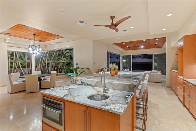 kitchen with sink, light stone counters, a spacious island, decorative light fixtures, and a kitchen bar