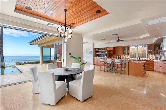 dining space featuring a water view, wooden ceiling, sink, and a tray ceiling