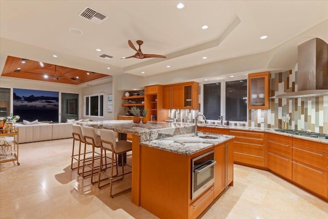 kitchen with a kitchen bar, appliances with stainless steel finishes, a tray ceiling, exhaust hood, and a large island