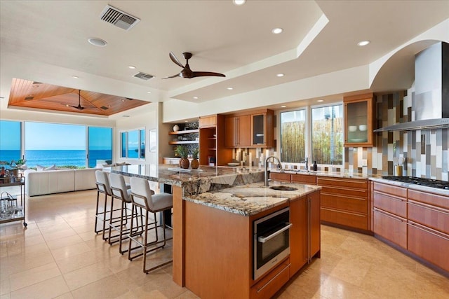 kitchen featuring a spacious island, a water view, island exhaust hood, a tray ceiling, and stainless steel appliances