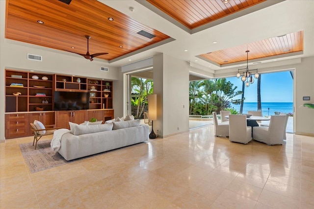 tiled living room with ceiling fan with notable chandelier, a water view, a raised ceiling, and wooden ceiling