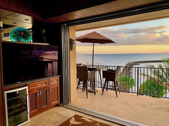 interior space with wine cooler, a balcony, a water view, and a beach view