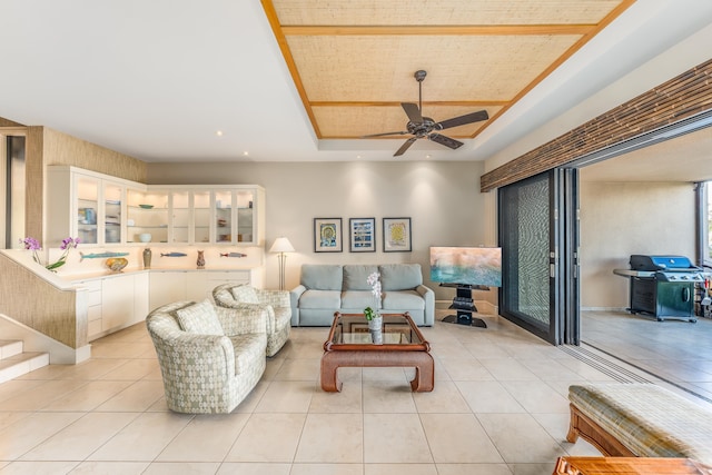 living room with light tile patterned floors, ceiling fan, and a tray ceiling