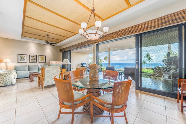 tiled dining space featuring a raised ceiling, ceiling fan with notable chandelier, and a water view