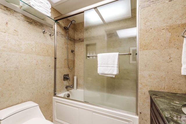 full bathroom with bath / shower combo with glass door, tile walls, toilet, and vanity