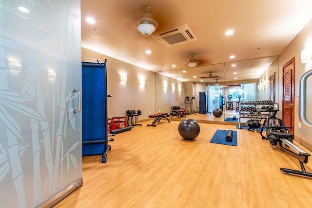 exercise room with a barn door, ceiling fan, and light hardwood / wood-style flooring