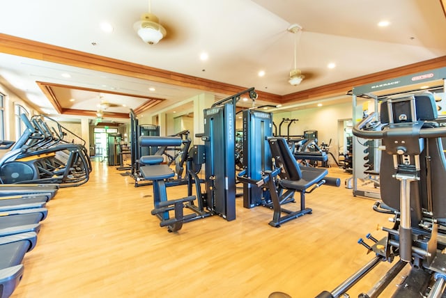 gym featuring crown molding, ceiling fan, a tray ceiling, and light wood-type flooring