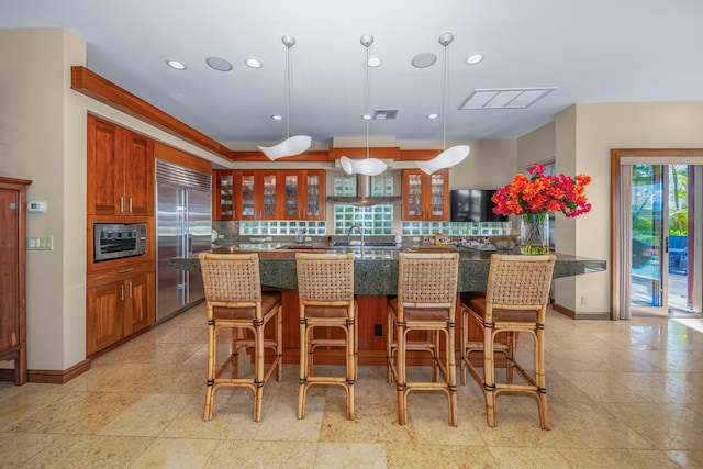 kitchen featuring kitchen peninsula, sink, built in appliances, decorative light fixtures, and a breakfast bar area