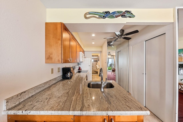 kitchen featuring kitchen peninsula, ceiling fan, light stone countertops, sink, and white appliances