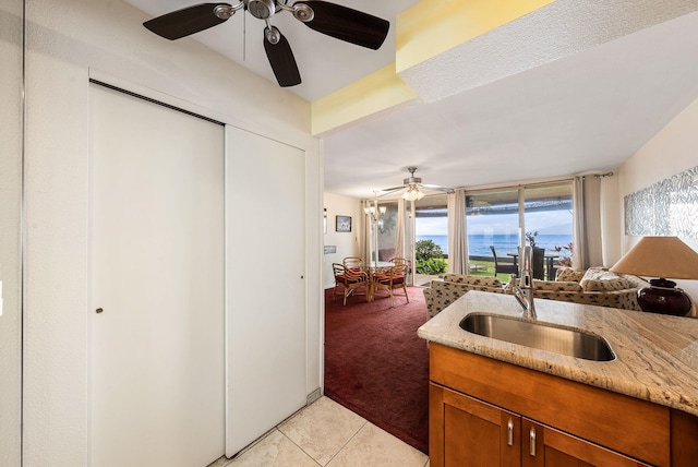 kitchen featuring sink, light stone countertops, light colored carpet, a water view, and ceiling fan