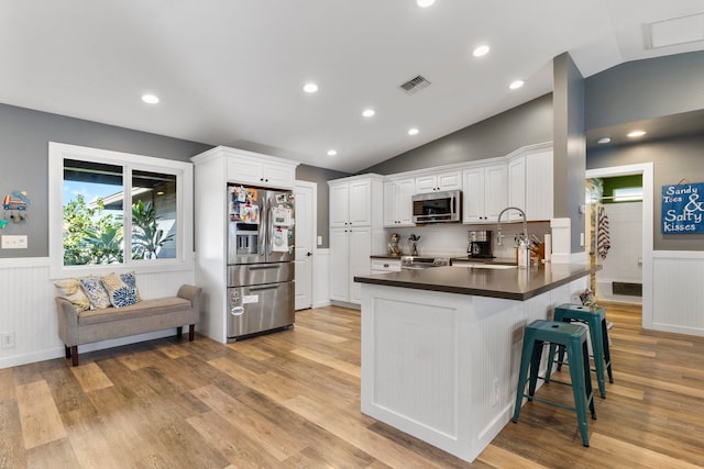 kitchen with kitchen peninsula, vaulted ceiling, stainless steel appliances, and white cabinets