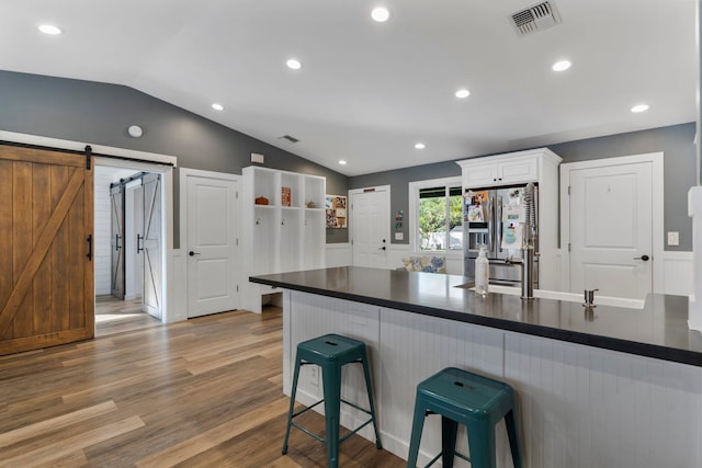 kitchen with stainless steel fridge, white cabinetry, hardwood / wood-style flooring, a barn door, and vaulted ceiling