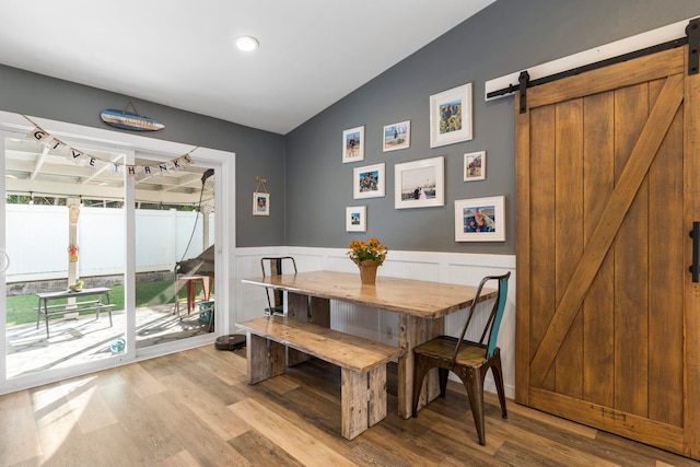 dining space with a barn door, vaulted ceiling, and light hardwood / wood-style flooring