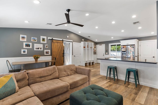 living room with ceiling fan, light hardwood / wood-style floors, a barn door, and lofted ceiling