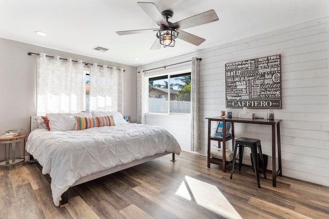 bedroom featuring ceiling fan, wooden walls, and hardwood / wood-style floors