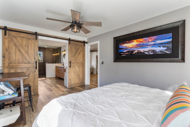 bedroom featuring light hardwood / wood-style flooring, ceiling fan, ensuite bathroom, and a barn door