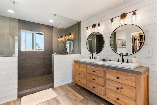 bathroom featuring wood-type flooring, wood walls, vanity, and tiled shower