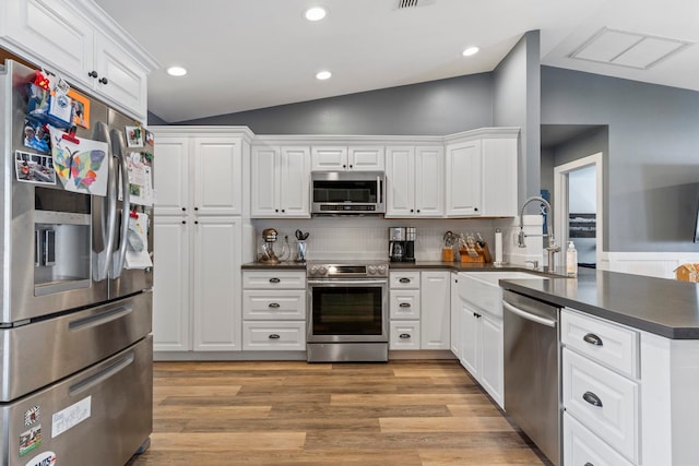 kitchen with lofted ceiling, kitchen peninsula, light hardwood / wood-style flooring, white cabinetry, and stainless steel appliances