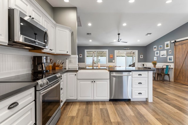 kitchen featuring light hardwood / wood-style floors, white cabinets, kitchen peninsula, a barn door, and stainless steel appliances