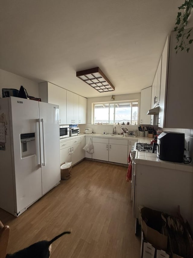 kitchen featuring sink, white appliances, light hardwood / wood-style flooring, white cabinets, and tile countertops