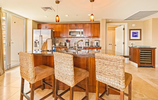 kitchen featuring light tile patterned flooring, stainless steel appliances, a kitchen island with sink, and pendant lighting