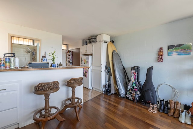 kitchen with dark hardwood / wood-style floors, white refrigerator, kitchen peninsula, a breakfast bar, and white cabinets