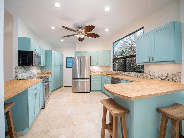 kitchen featuring a kitchen bar, tasteful backsplash, stainless steel appliances, blue cabinets, and butcher block countertops