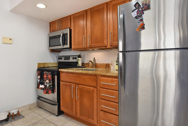 kitchen with appliances with stainless steel finishes, sink, light stone counters, and light tile patterned flooring