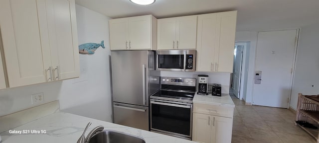 kitchen with white cabinetry, stainless steel appliances, light stone countertops, and light tile patterned floors