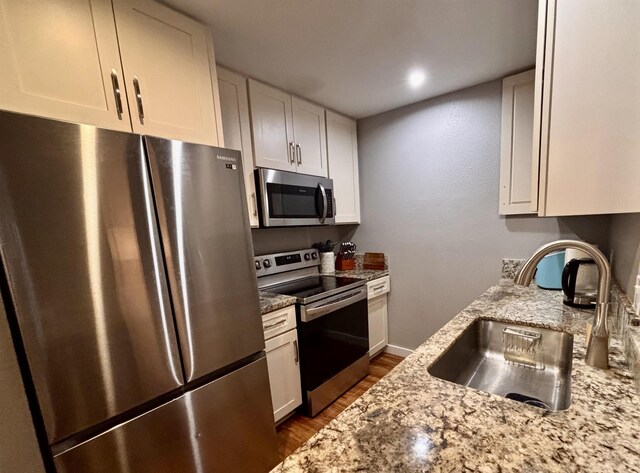 kitchen with stainless steel appliances, dark wood-type flooring, white cabinetry, a sink, and light stone counters