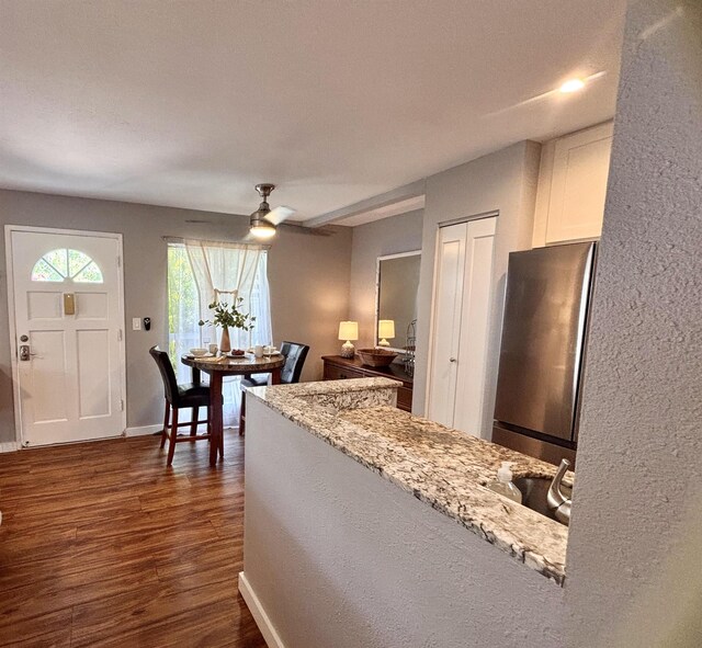 kitchen with baseboards, dark wood-style floors, light stone counters, freestanding refrigerator, and white cabinets