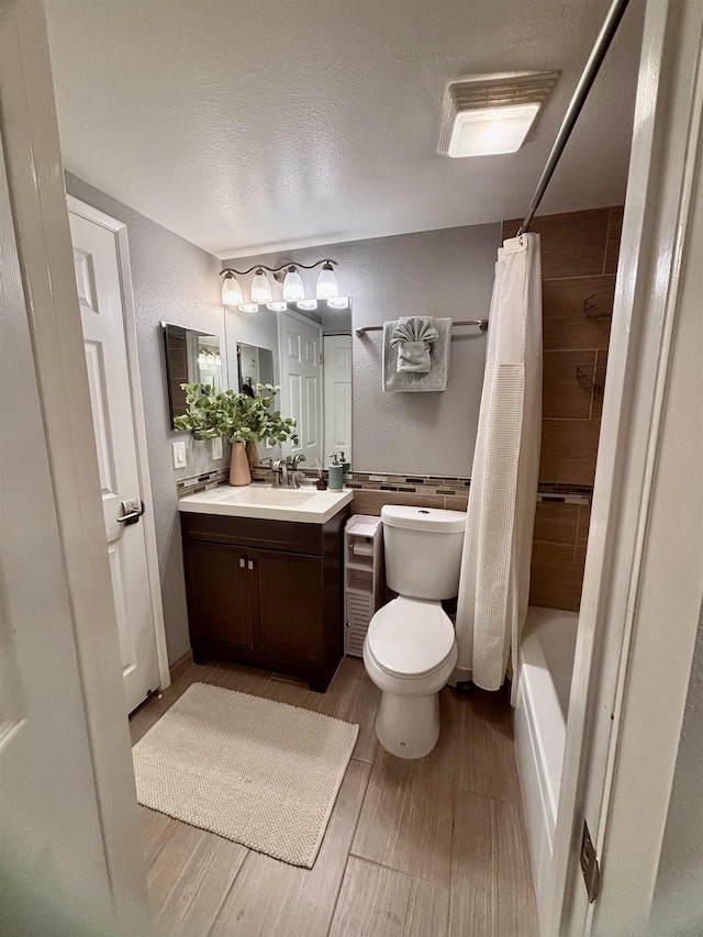 bathroom with toilet, vanity, wood tiled floor, shower / tub combo with curtain, and a textured wall