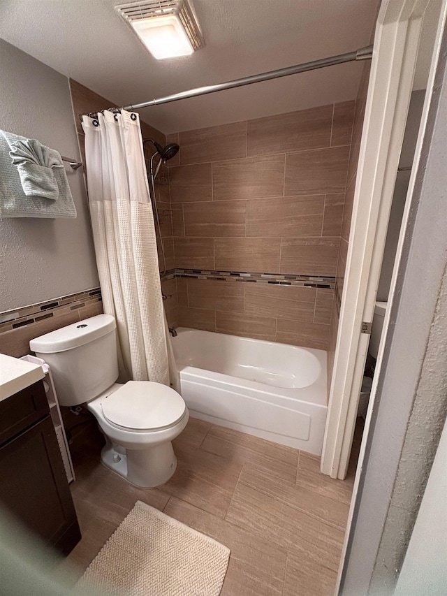 bathroom featuring visible vents, toilet, vanity, shower / tub combo with curtain, and a textured wall