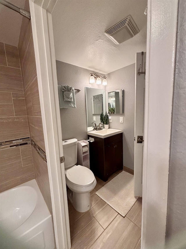 bathroom with a textured ceiling, visible vents, toilet, vanity, and a textured wall