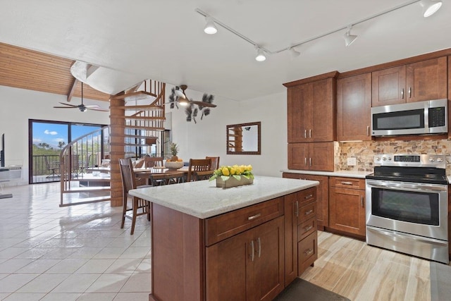 kitchen with a kitchen island, appliances with stainless steel finishes, decorative backsplash, light tile patterned floors, and light stone countertops