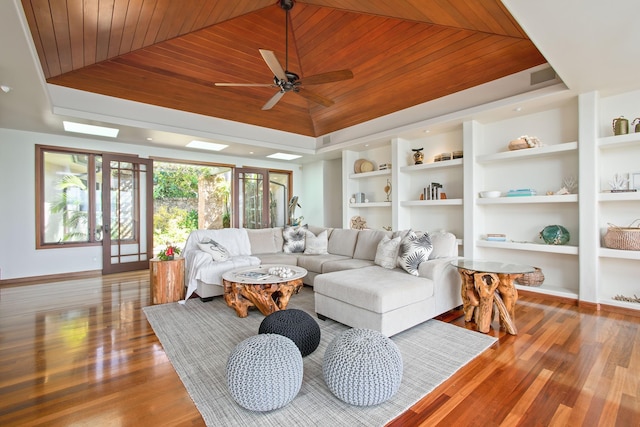 living area featuring built in shelves, wood ceiling, baseboards, light wood-type flooring, and a raised ceiling