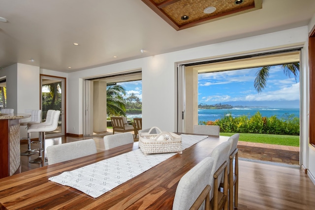 dining area featuring a water view, hardwood / wood-style flooring, and a tray ceiling