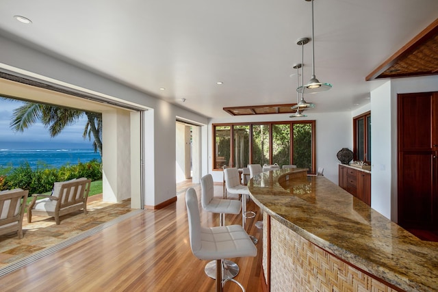 kitchen featuring a water view, stone counters, light hardwood / wood-style floors, and decorative light fixtures