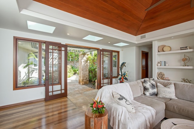 living room featuring lofted ceiling with skylight, built in shelves, light hardwood / wood-style flooring, and wooden ceiling