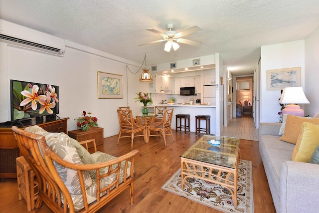 living room featuring ceiling fan, a textured ceiling, hardwood / wood-style floors, and a wall mounted air conditioner