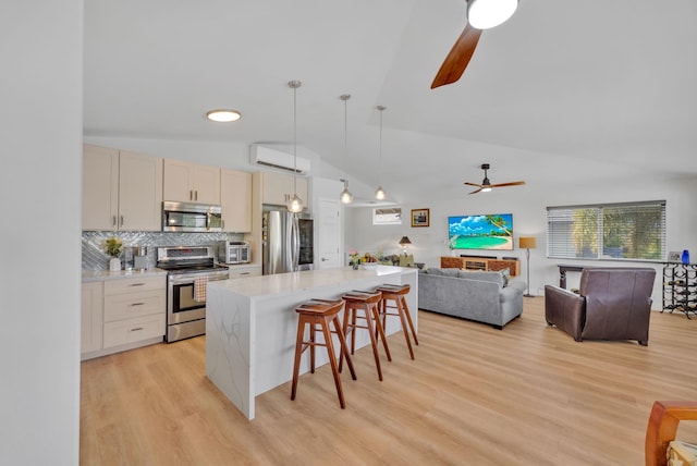 kitchen with a breakfast bar area, stainless steel appliances, a kitchen island, light wood-type flooring, and a wall mounted air conditioner