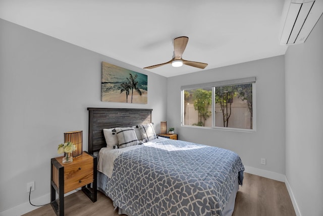 bedroom featuring a ceiling fan, an AC wall unit, baseboards, and wood finished floors