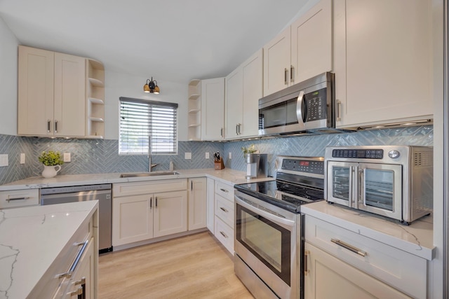 kitchen featuring decorative backsplash, light wood-style flooring, stainless steel appliances, open shelves, and a sink