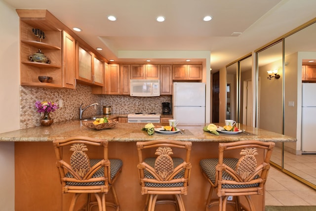 kitchen featuring kitchen peninsula, white appliances, light tile flooring, tasteful backsplash, and light stone counters