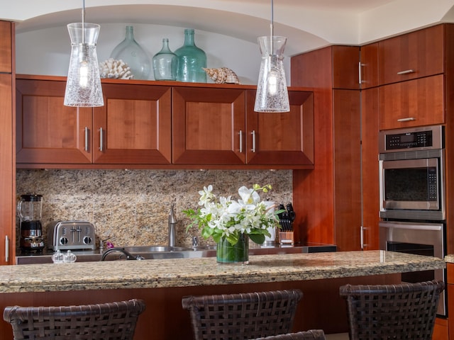 kitchen with decorative backsplash, stainless steel double oven, decorative light fixtures, and sink