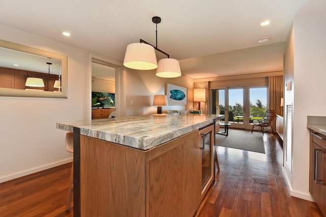 kitchen featuring a breakfast bar, a center island, hanging light fixtures, dark hardwood / wood-style floors, and light stone countertops