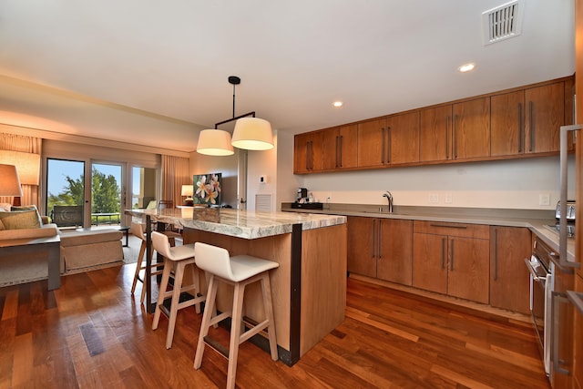 kitchen featuring pendant lighting, a center island, dark wood-type flooring, a kitchen breakfast bar, and sink