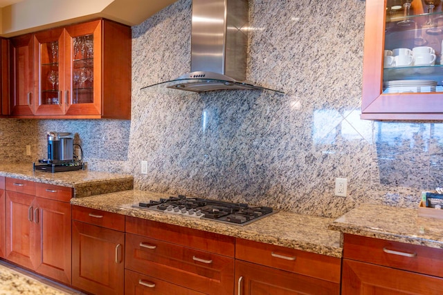 kitchen with wall chimney exhaust hood, stainless steel gas stovetop, backsplash, and light stone countertops