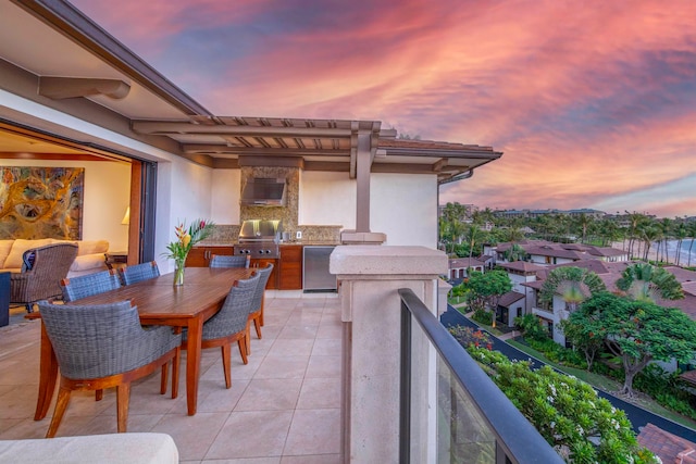 patio terrace at dusk featuring grilling area, a balcony, and exterior kitchen