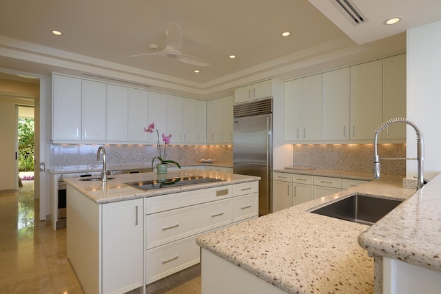 kitchen with built in refrigerator, light stone countertops, sink, and cooktop